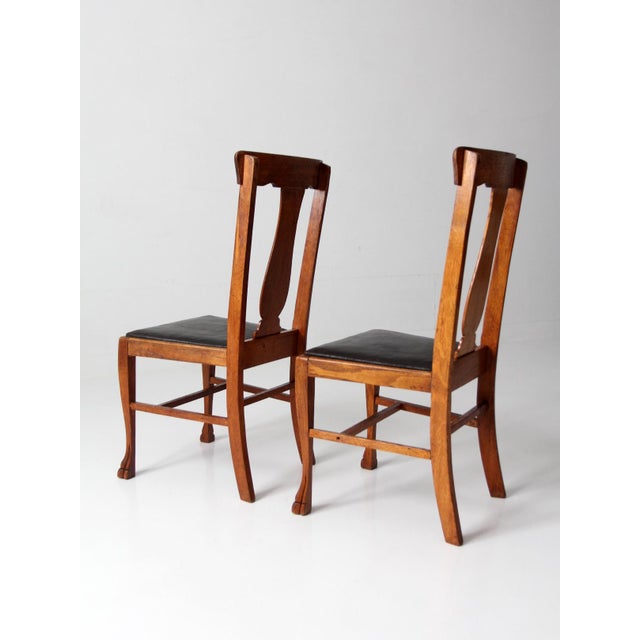 Pair of 1930s oak splat back side chairs with carved claw feet and black faux leather seats. The tall backs and shaped...