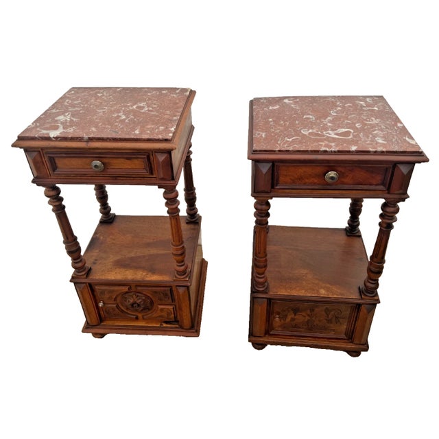 Stunning matched pair of antique European bedside cabinets featuring rich walnut frames topped with striking variegated...