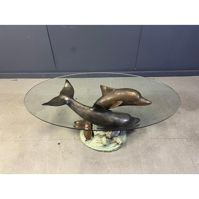 A mid century french bronze swimming dolphins sculpturetable base supporting a beveled clear glass top creates an elegant...