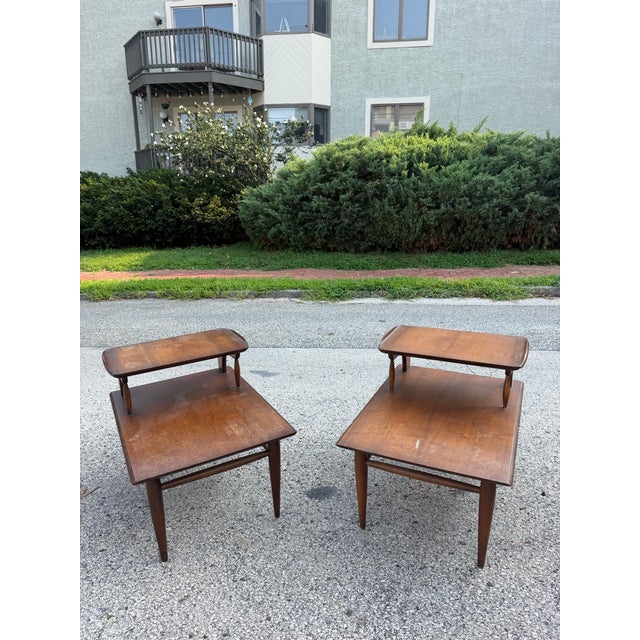 A pair of mid century Bassett Furniture side tables. The tables are two tiered. Dimensions: H: 22.25” W: 21” D: 29.5” Tier...