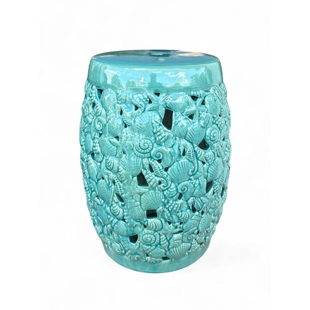 The Aqua Garden Stool is a ceramic garden stool with a barrel form covered in a sculpted seashell and seahorse motif with...