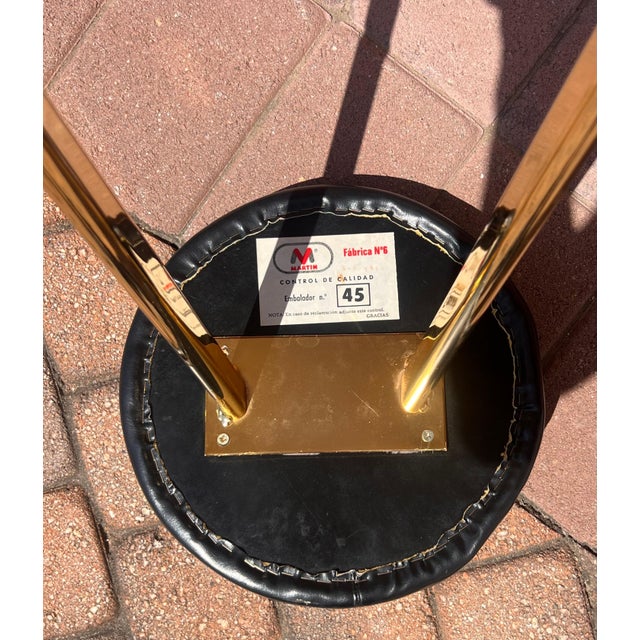 A set of three vintage postmodern bar or counter stool featuring gilt metal frames and faux leather seating, probably...