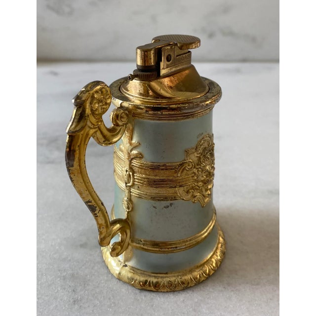 Vintage mid century ornate table lighter with gold and metallic baby blue finish. Scroll handle and lion emblem on either...