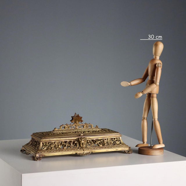Elongated rectangular inkwell in gilded and carved bronze. Decorated with scrolls, plant motifs, and masks. A double...