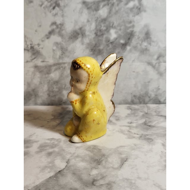A charming secretive ceramic angel/cherub figurine is in a yellow jumpsuit. Sweet wings are handpainted with gold accents....