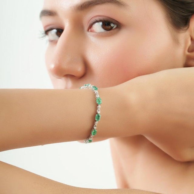 This elegant infinity link bracelet features 14 natural oval-cut emeralds totaling 6.76 carats, accented with 0.30 carats...