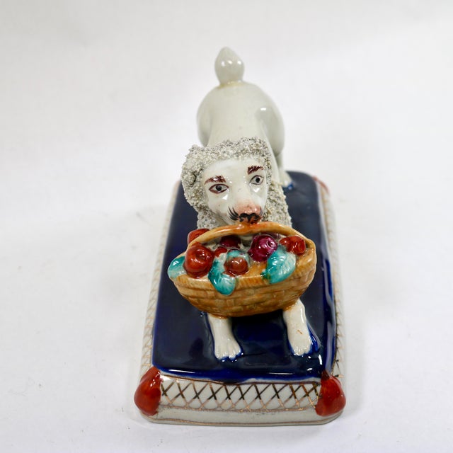Fantastic Victorian-era Staffordshire porcelain confetti poodle holding a basket of apples in its mouth. This dog is...