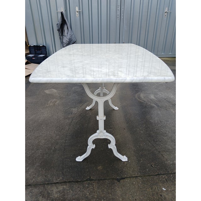 This is a classic French bistro table with generous proportions. The base is made of wrought iron, painted white, and the...