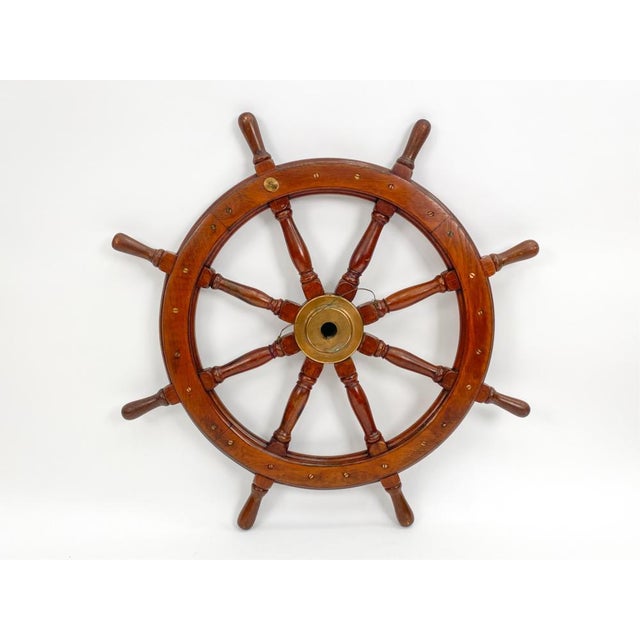 A vintage wooden ship's steering wheel in a warm reddish-brown hardwood mahogany with ten turned spokes extending past the...