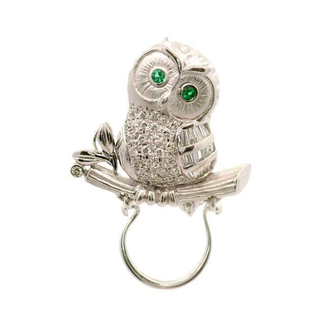 A contemporary brooch featuring a whimsical owl design, perched gracefully on a branch. The body is encrusted with round-...
