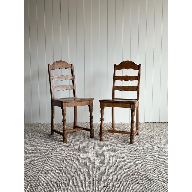 This antique pair of ladder-back chairs features scalloped slat backs, hand-turned front legs, and a beautifully timeworn...