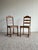 This antique pair of wooden dining chairs features a classic ladderback design with scalloped slats and beautiful timeworn...