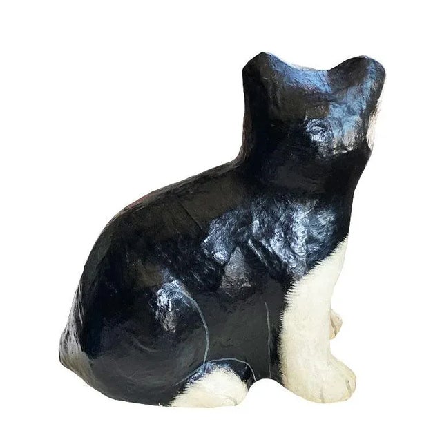 A black and white paper mache kitten sculpture. This fun figurine depicts a cat with white paws and nose, and a black...