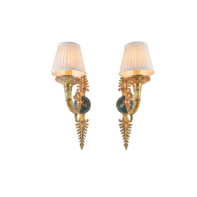Pair of French-style gilded brass wall sconces dating to the 1950s. Each has an ornamental scroll arm with feather-like...