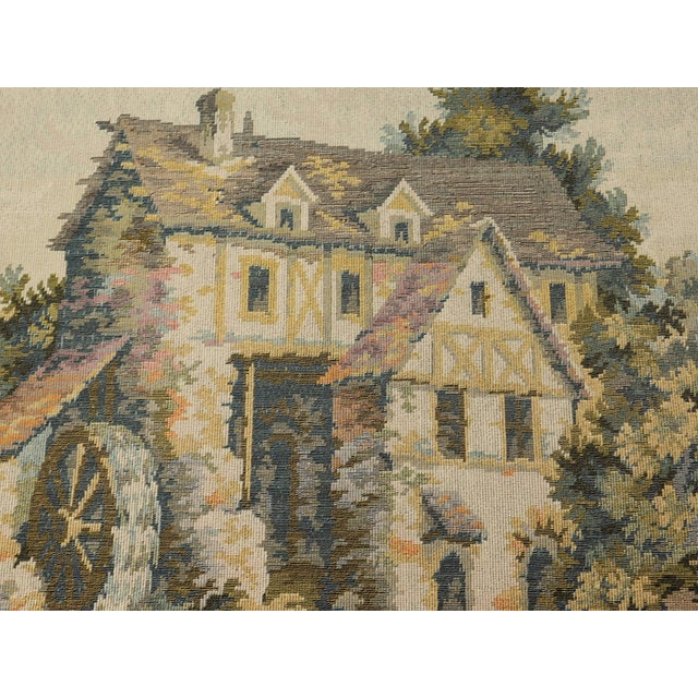 A vintage tapestry depicting a wooded scenery, with riverbank in the forefront and a residential monument in the background.