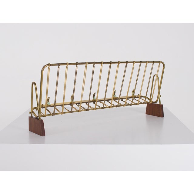 Wall-mounted coat rack in brass, brass-plated aluminum, and teak. The central storage compartment is organized by a series...