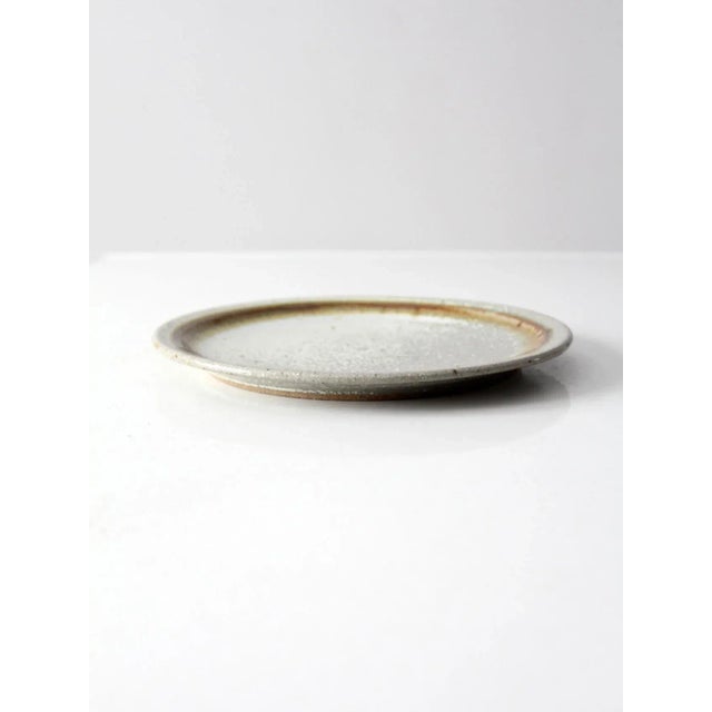 This is a vintage studio pottery plate. The hand-crafted dish feature a speckled gray and brown glaze.