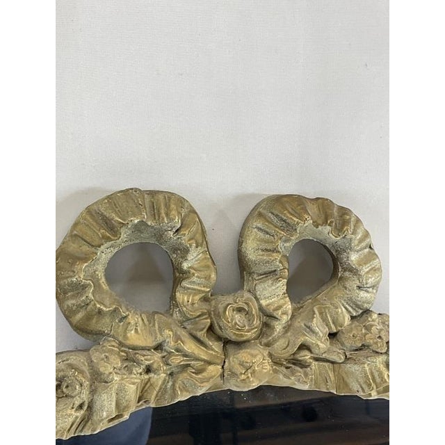 An elegant antique-style gilt wall mirror featuring a beautifully sculpted bow crest and intricate floral detailing...