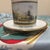 An antique-style porcelain cup and matching saucer featuring a detailed topographical view of the Schloss Charlottenburg...