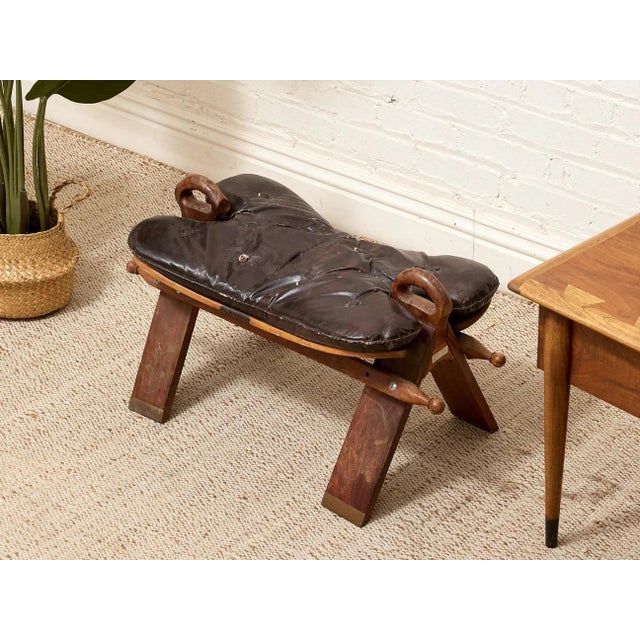 A distinctive vintage saddle stool featuring a deeply tufted black leather seat set on a substantial wood frame with...