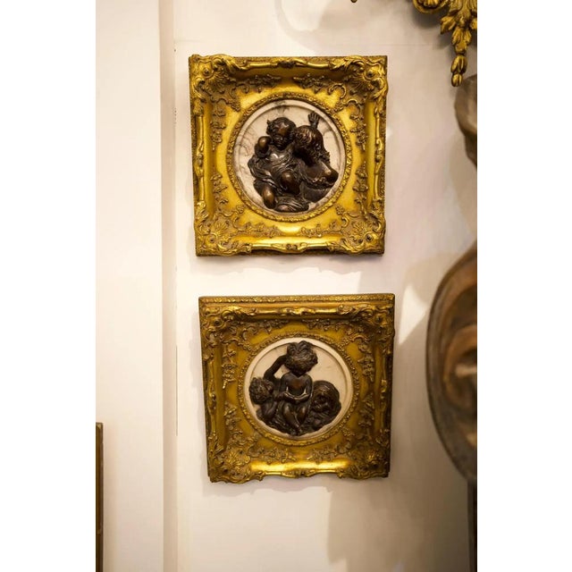 A pair of stunning French early 20th century marble, bronze and giltwood cameo wall art. Housed within an exuberantly...