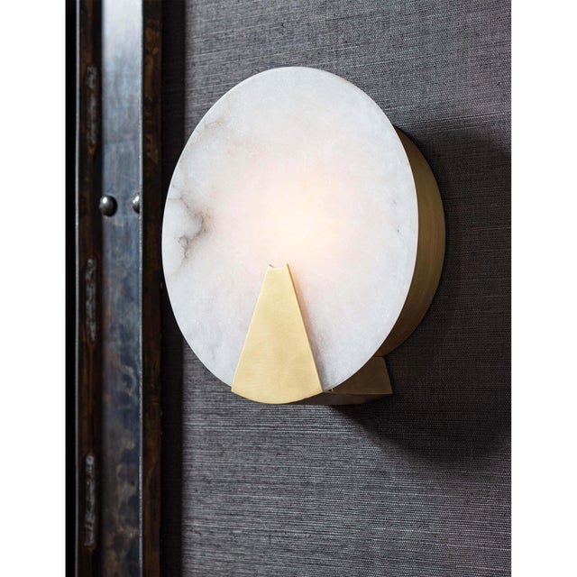 Houston sconce showcases a round piece of natural alabaster secured by natural brass-finished metal framing. Light shines...