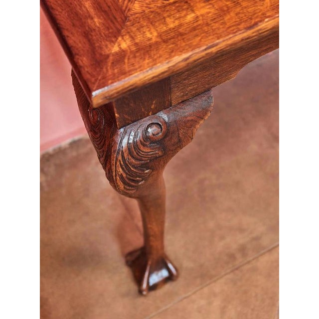 The solid oak console table is hand-carved in the English Chippendale style with a top decorated with parquetry. The legs...