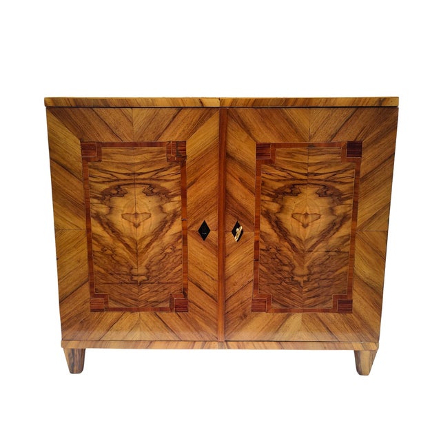 A beautifully crafted biedermeier-style half cabinet made around 1920, featuring exceptional walnut veneer in symmetrical...