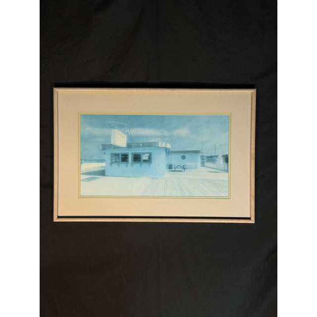 Large framed coastal boardwalk print featuring a soft blue beachside building scene with an airy, calm, and relaxed...