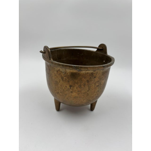 Heavy brass/cast brass kettle with three legs and a movable handle. The exterior has a distinct patina and signs of age,...