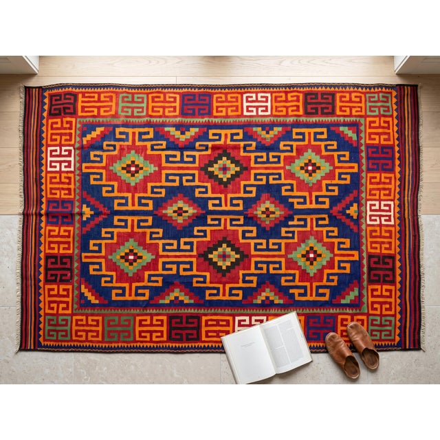 A handwoven Maimana kilim from northern Afghanistan on a deep indigo ground, worked with brilliant orange, crimson,...