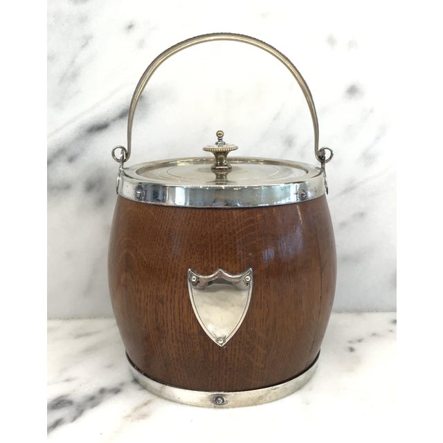 English oak biscuit barrel which retains its original porcelain liner and is decorated with a silverplate crest. DETAILS...