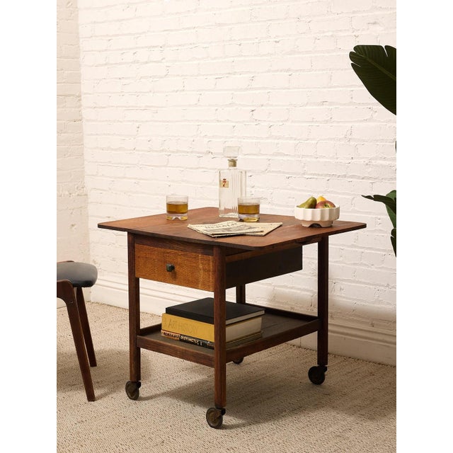 A wonderfully practical vintage rolling table with warm oak tones and a compact, utilitarian silhouette. The top is framed...