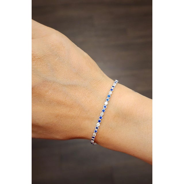 This elegant tennis bracelet embodies modern sophistication. Featuring a harmonious blend of natural round-cut blue...