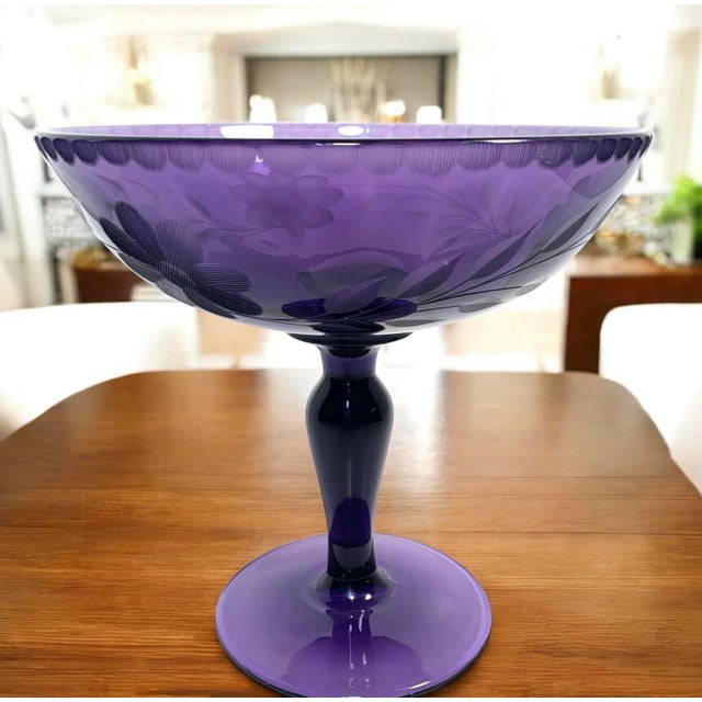 This late 19th to early 20th century amethyst glass compote features an etched floral motif, resting on a tall stemmed...