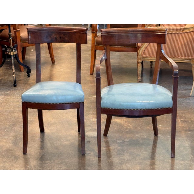 A set of seven klismos chairs showing the classic curved crest rail and gently splayed saber legs of the form. The...