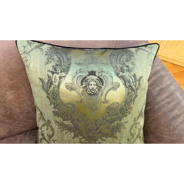 A woven cushion cover centered on a classical Medusa portrait, surrounded by scrolling acanthus motifs and winged putti...
