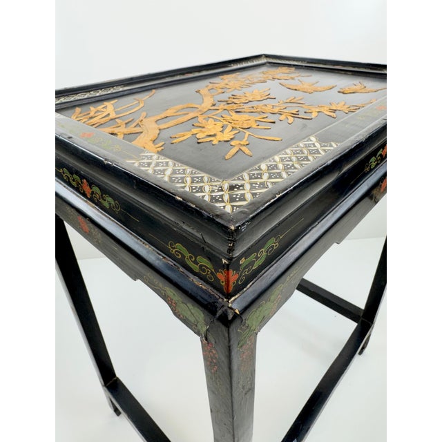 A striking vintage Chinoiserie side table featuring a rich black lacquer-style finish and an ornate raised decorative top....