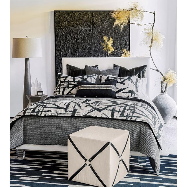 Upholstered in a luxurious ivory fabric, this cube ottoman exudes sophistication, while its vegan leather harness accents...