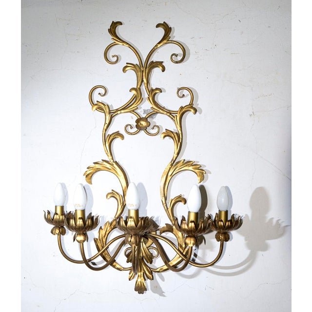 This gilded wrought-iron wall sconce is an elegant expression of classic decorative style, reminiscent of the creations of...