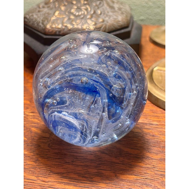 A vintage Murano art glass paperweight featuring dramatic cobalt blue and white ribbon inclusions suspended within clear...