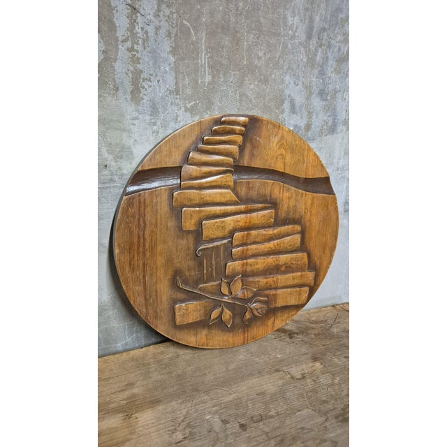 A distinctive vintage carved wooden wall plaque featuring a circular form with a raised sculptural relief. The composition...