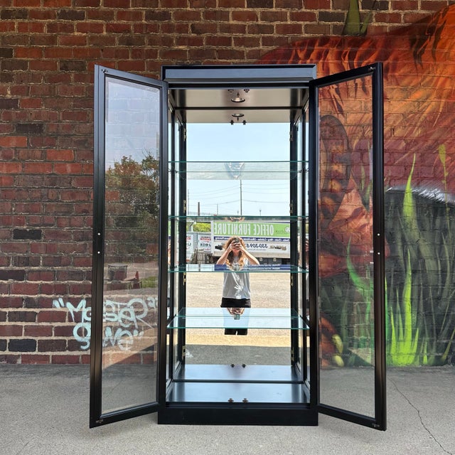 .This beautiful display cabinet by Jasper Cabinet features an eye catching semi-gloss black finish with contrasting brass...