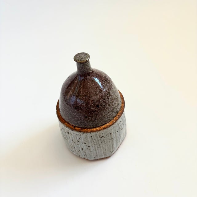 A vintage handmade studio pottery lidded container. Finished in speckled two toned glazes. The top is a grayish purple...