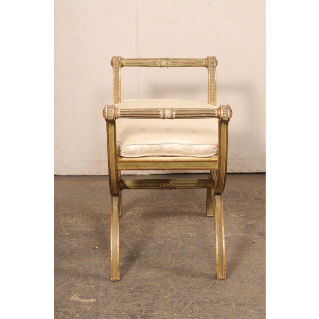 An Italian carved-wood curule stool, with upholstered seat, from the mid 20th century. This mid-century stool from Italy...