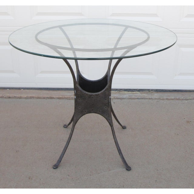 Round glass top table with industrial style metal base. The French garden style table has a heavy metal base in an...