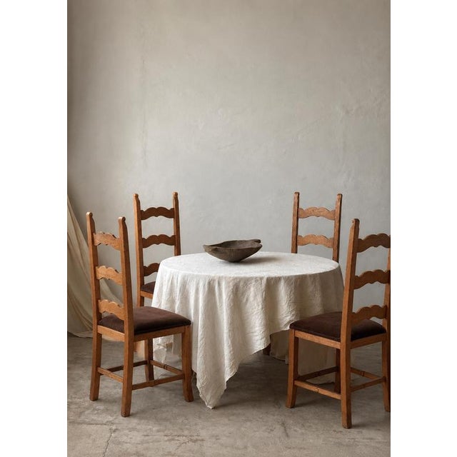 A matching set of four carved oak dining chairs with tall, slender ladder backs and three distinctive scalloped cross...