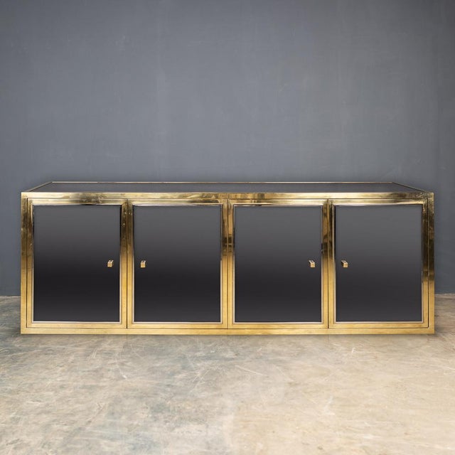 A large mirrored credenza / sideboard designed by Michel Pigneres, with four brass and chrome cupboard doors with mirrored...