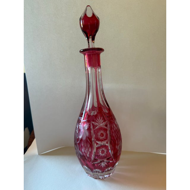 A beautifully cut wine decanter in rich cranberry cased over clear crystal, the slender baluster body deep-cut with grape...