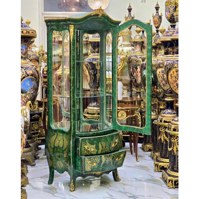 This elegant French-style vitrine cabinet features a rich green finish accented with intricate gold leaf detailing,...